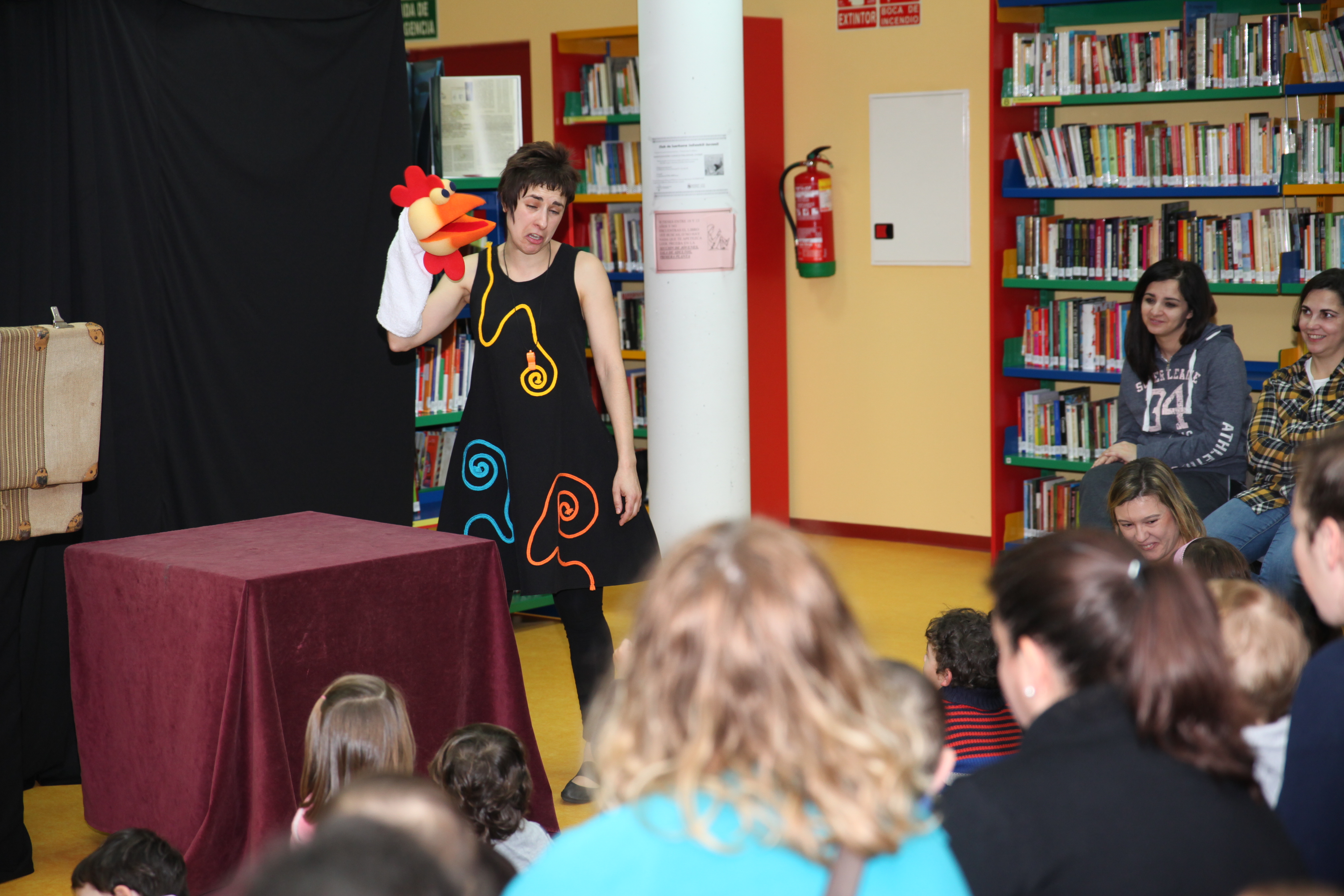 Niños pequeños y mamás  asisten a una sesión de cuentacuentos en una sala de biblioteca 