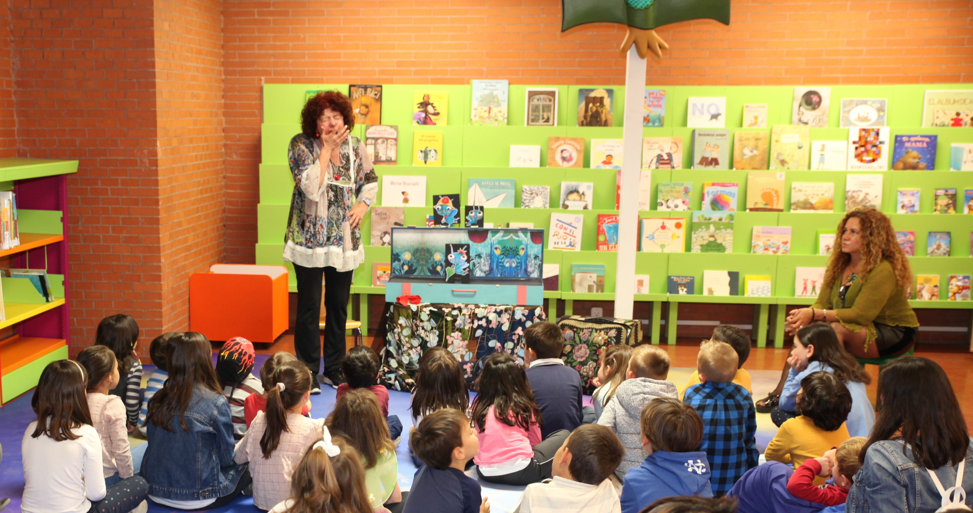 Una señora mayor de pie frente a una docena des niños y niñas sentados 