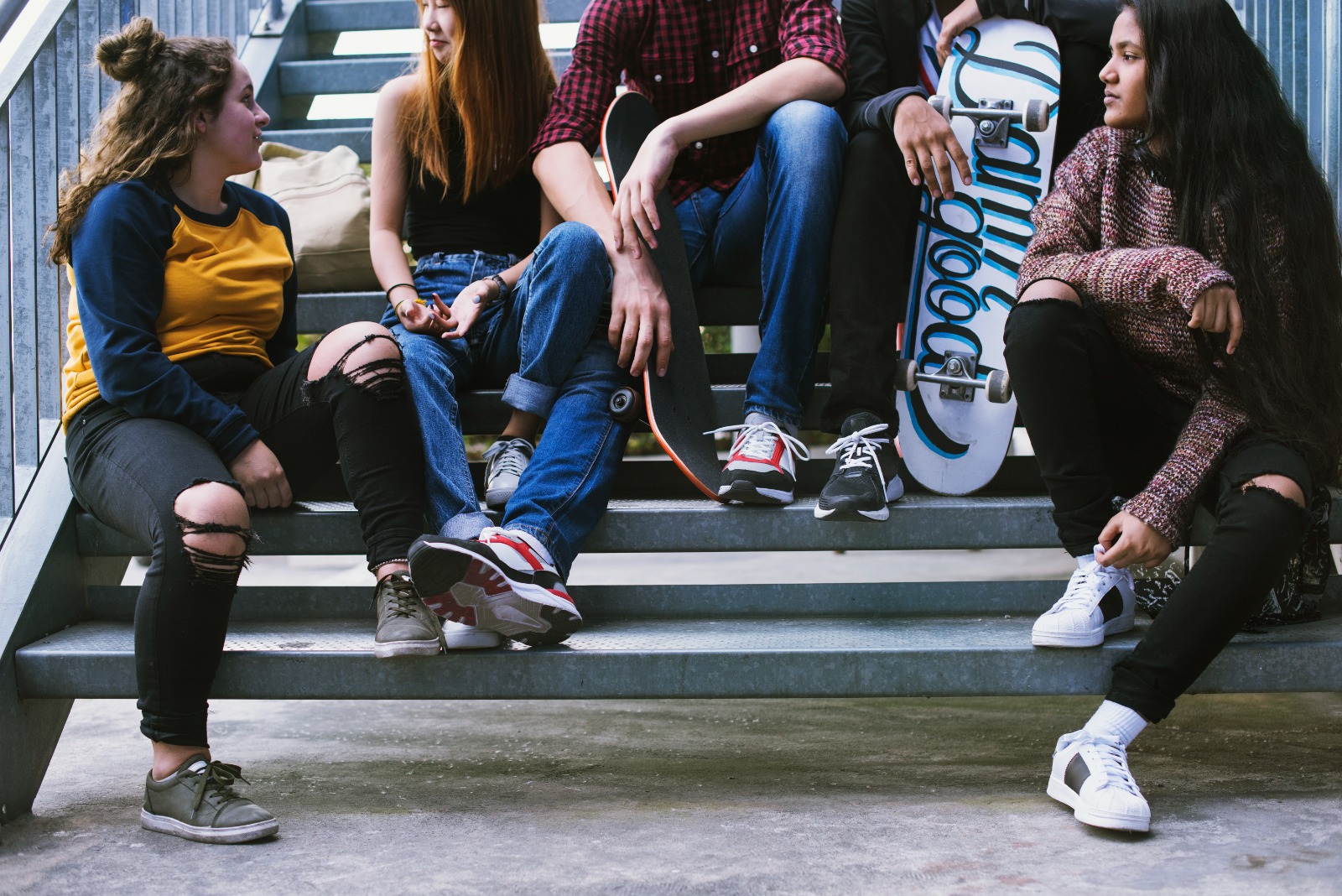 Grupo de 5 chicos y chicas sentados en una escalera al aire libre