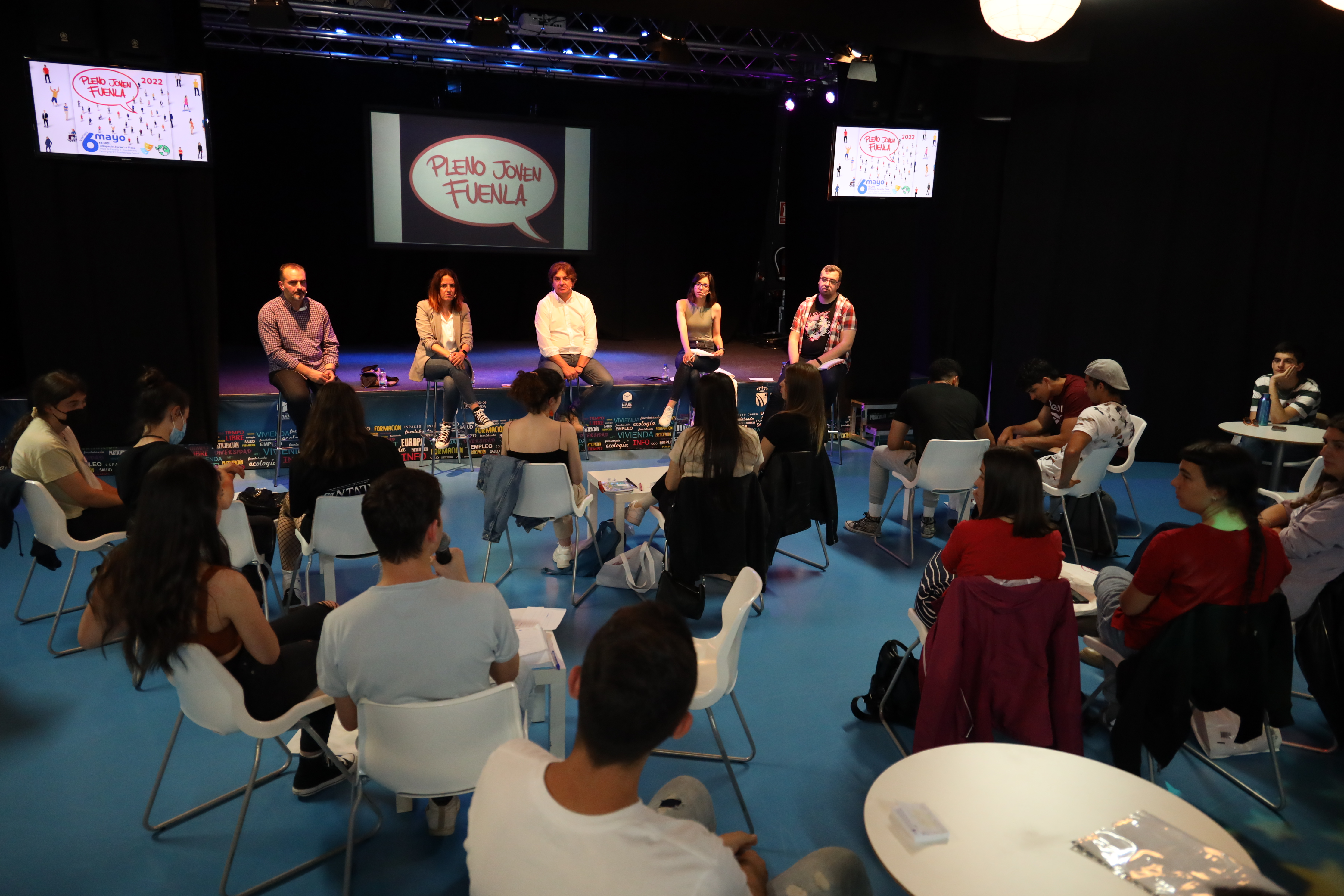 Jóvenes sentados mirando a cinco adultos en una sala 