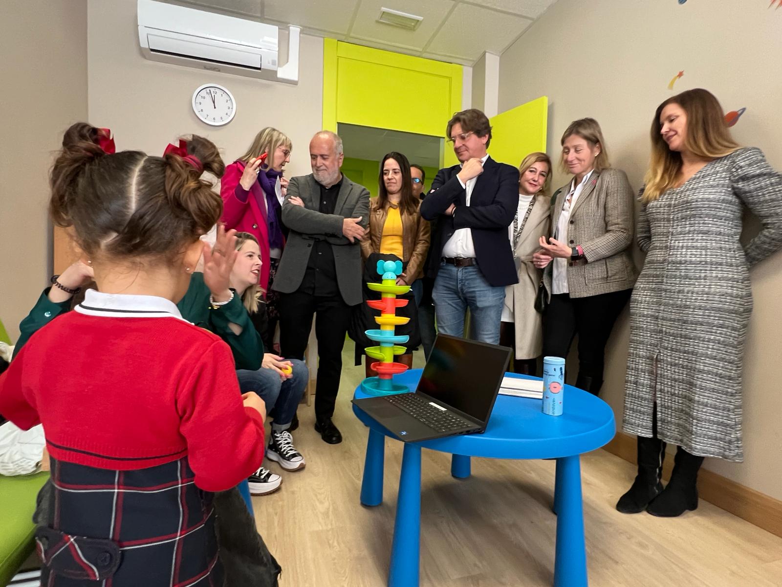 Media docena de hombres y mujeres en una habitación con una niña pequeña que juega sobre una mesa