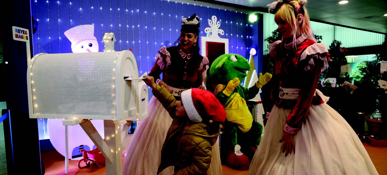 Un niño deposita una carta en un buzón decorado de Navidad