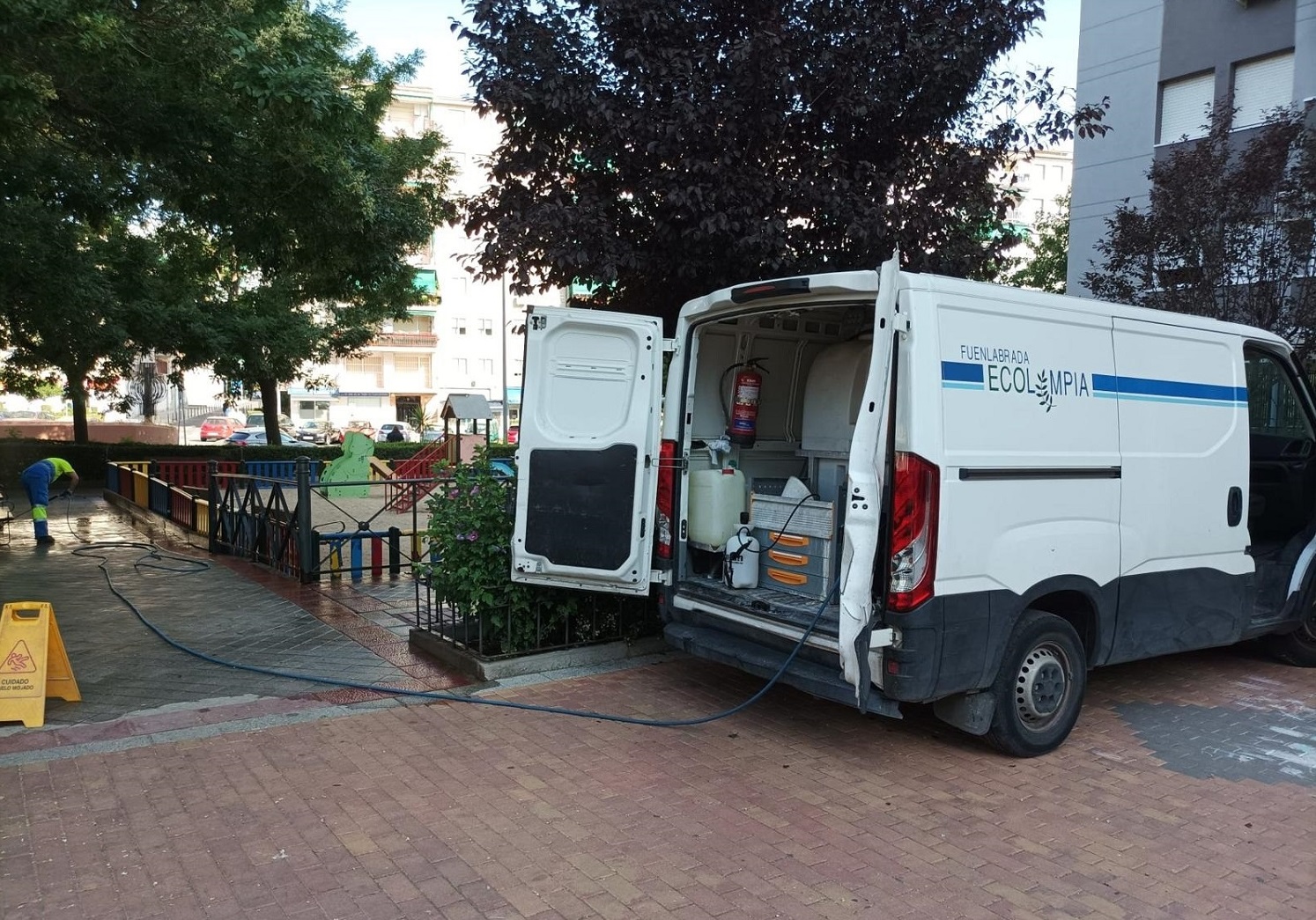 Operario de limpieza viaria con vehículo y equipo limpiando una acera