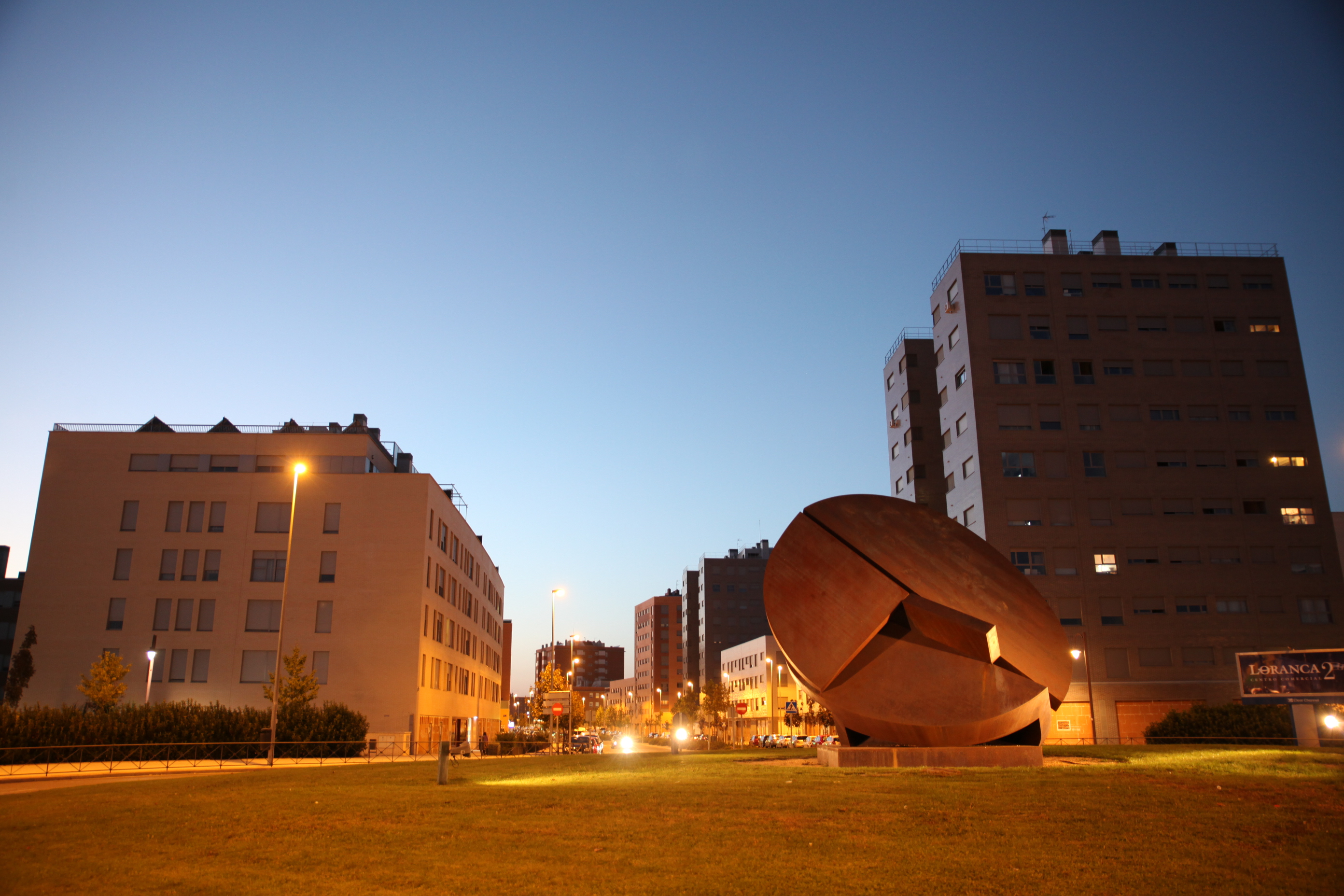 Edificios de viviendas y escultura redonda al atardecer con alumbrado encendido