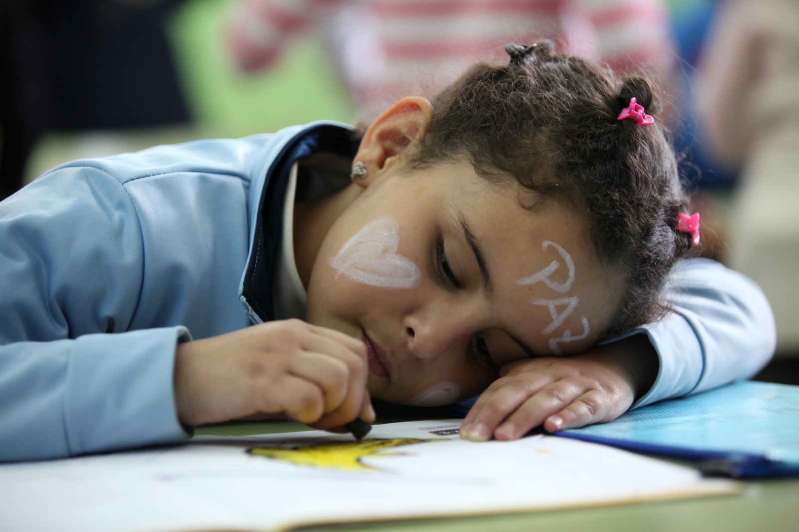 Niña en aula con la palabra PAZ escrita en la frente