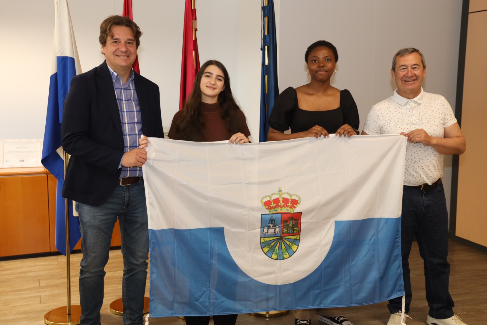 Dos chicas adolescentes y dos hombres sosteniendo una bandera blanca y azul con escudo