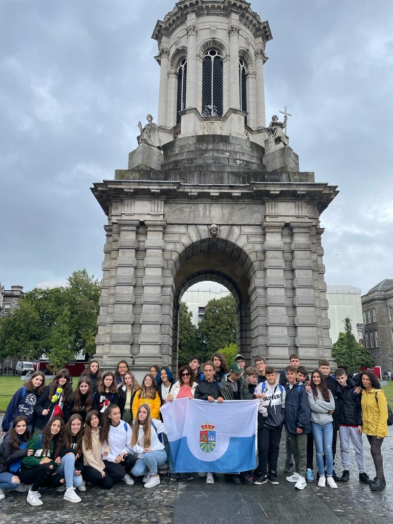 Grupo de adolescentes posando con una bandera de Fuenlabrada delante de una puerta monumental