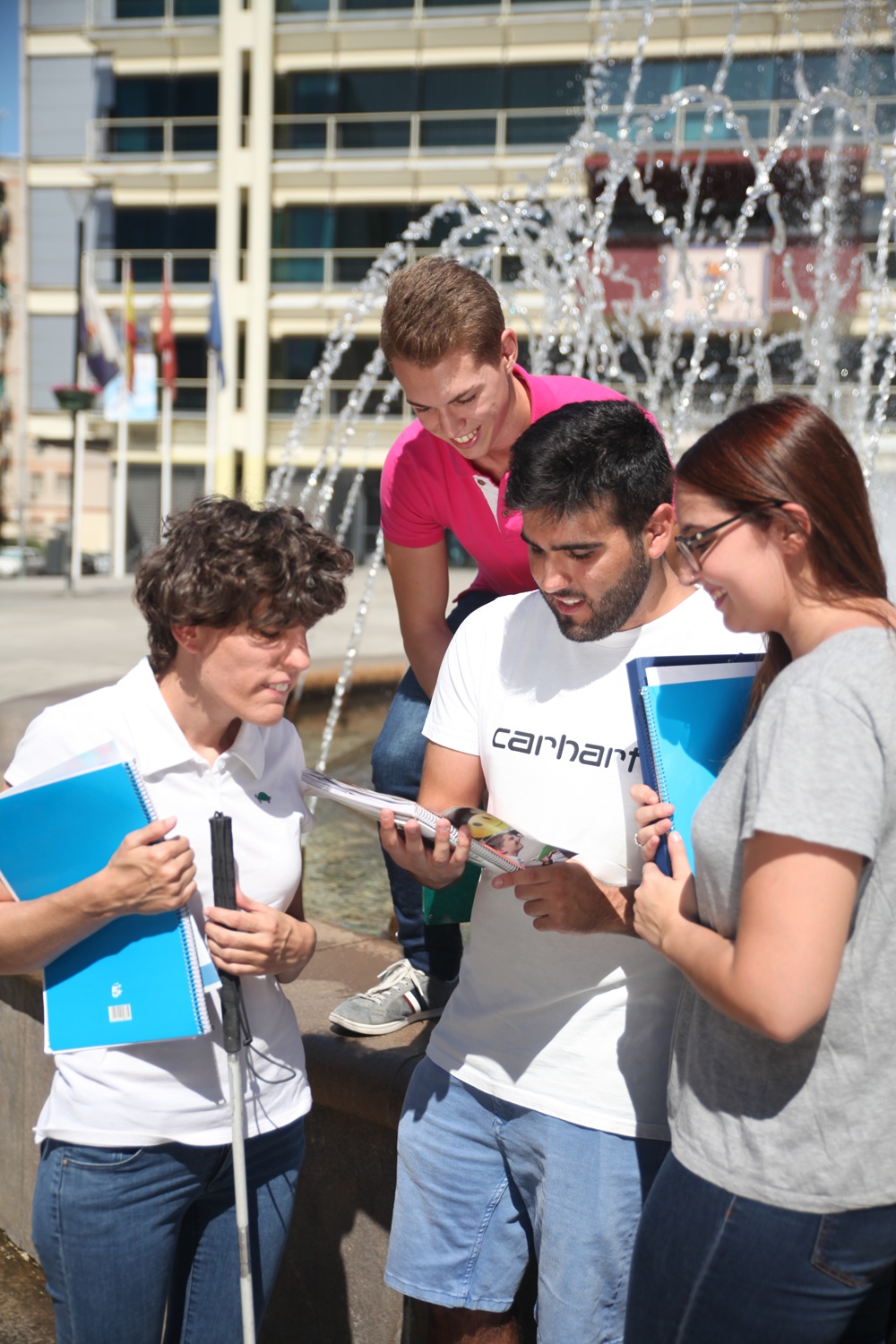 Cuatro jóvenes estudiantes consultan un cuaderno en la plaza de la Constitución