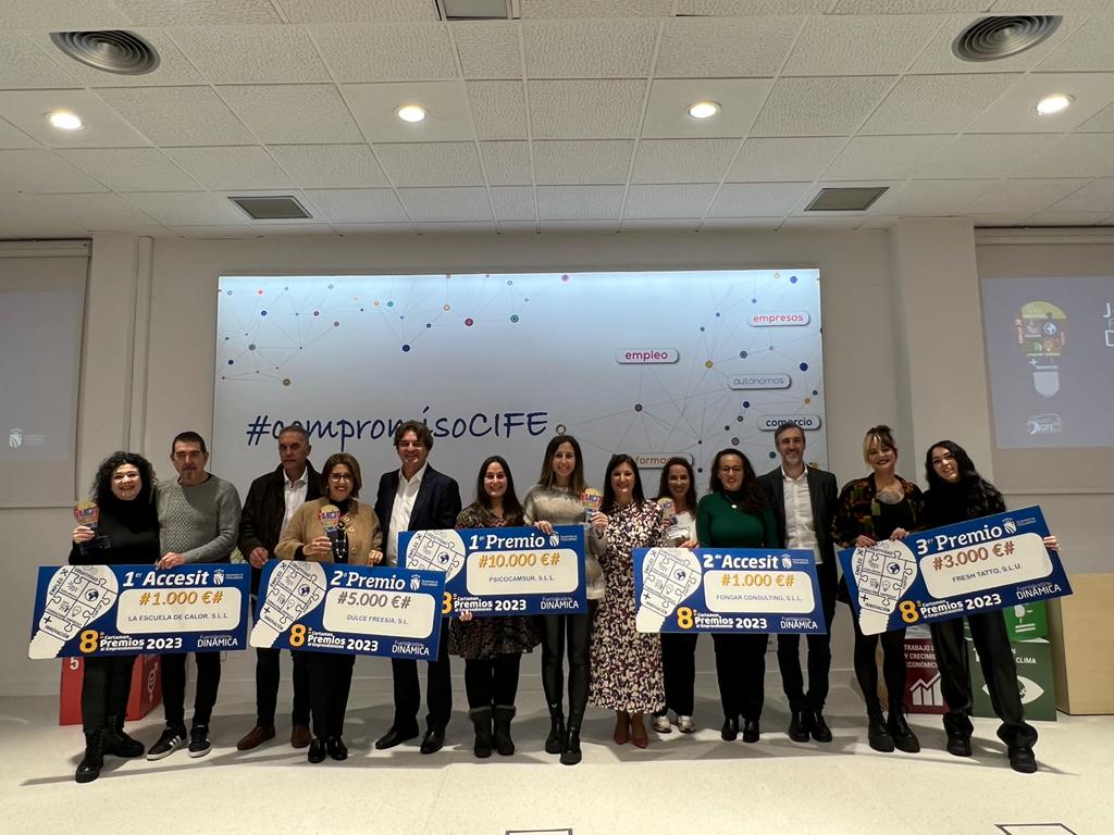 Una docena de hombres y mujeres en un escenario con carteles con forma de cheques 