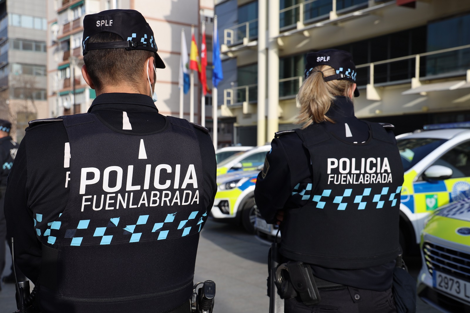 Un hombre y una mujer policías de espaldas y en sus trajes se lee Policía Local de Fuenlabrada