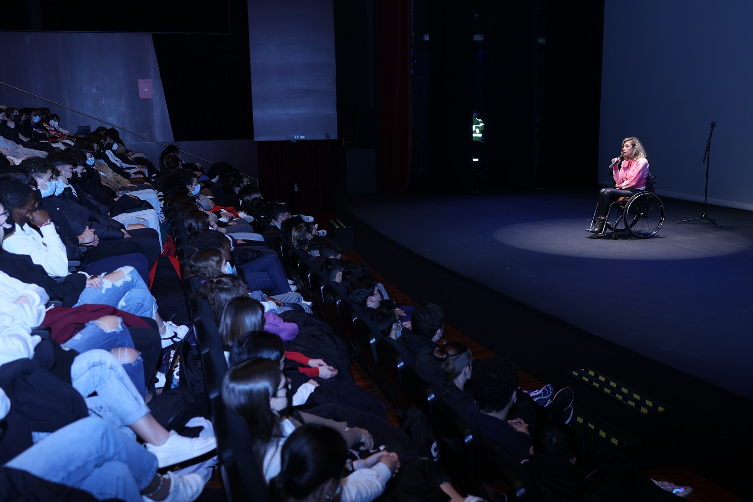 Estudiantes en un teatro y en el escenario una persona en silla de ruedas