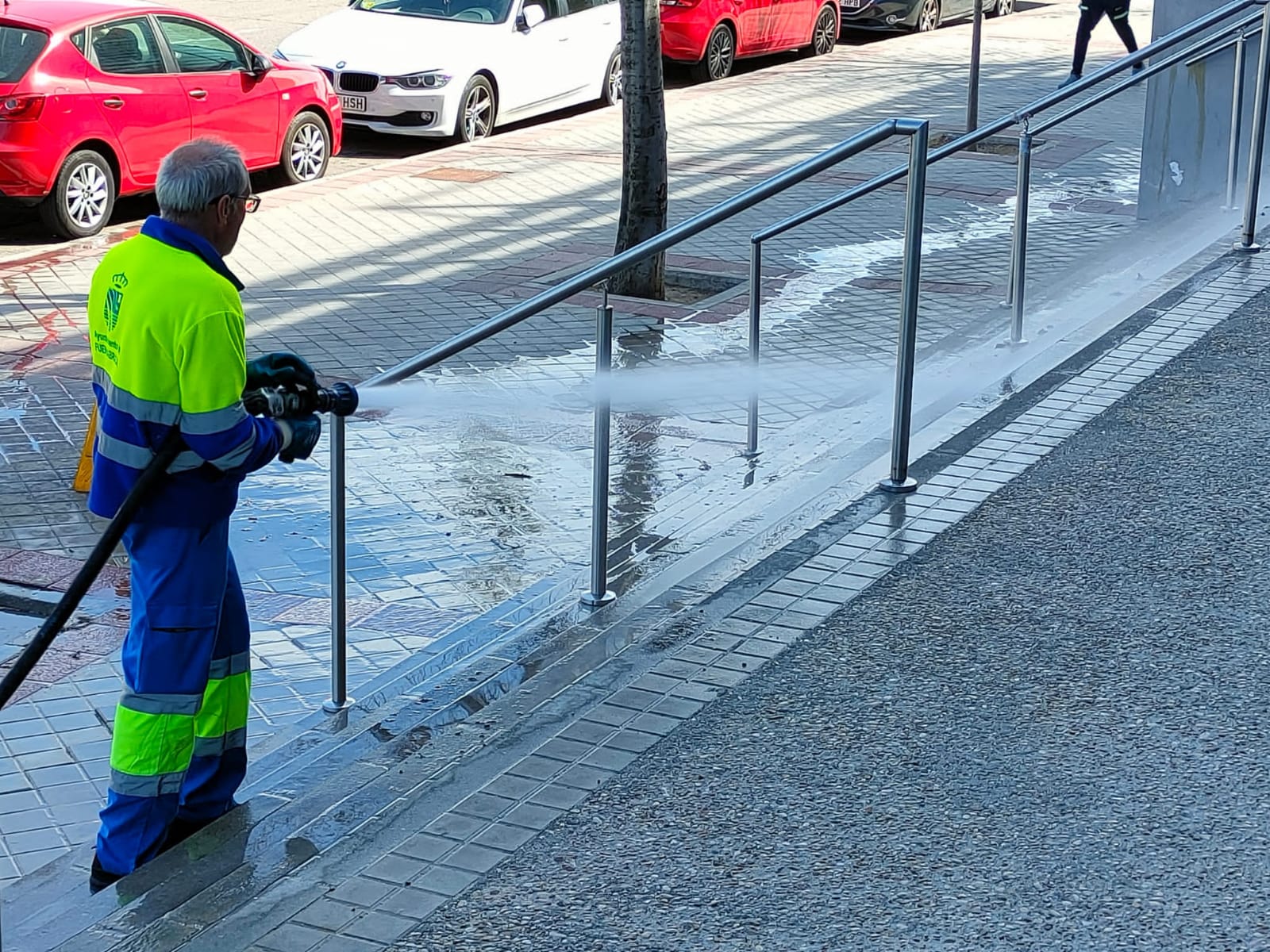 Operario de limpieza con una manguera limpiando la acera