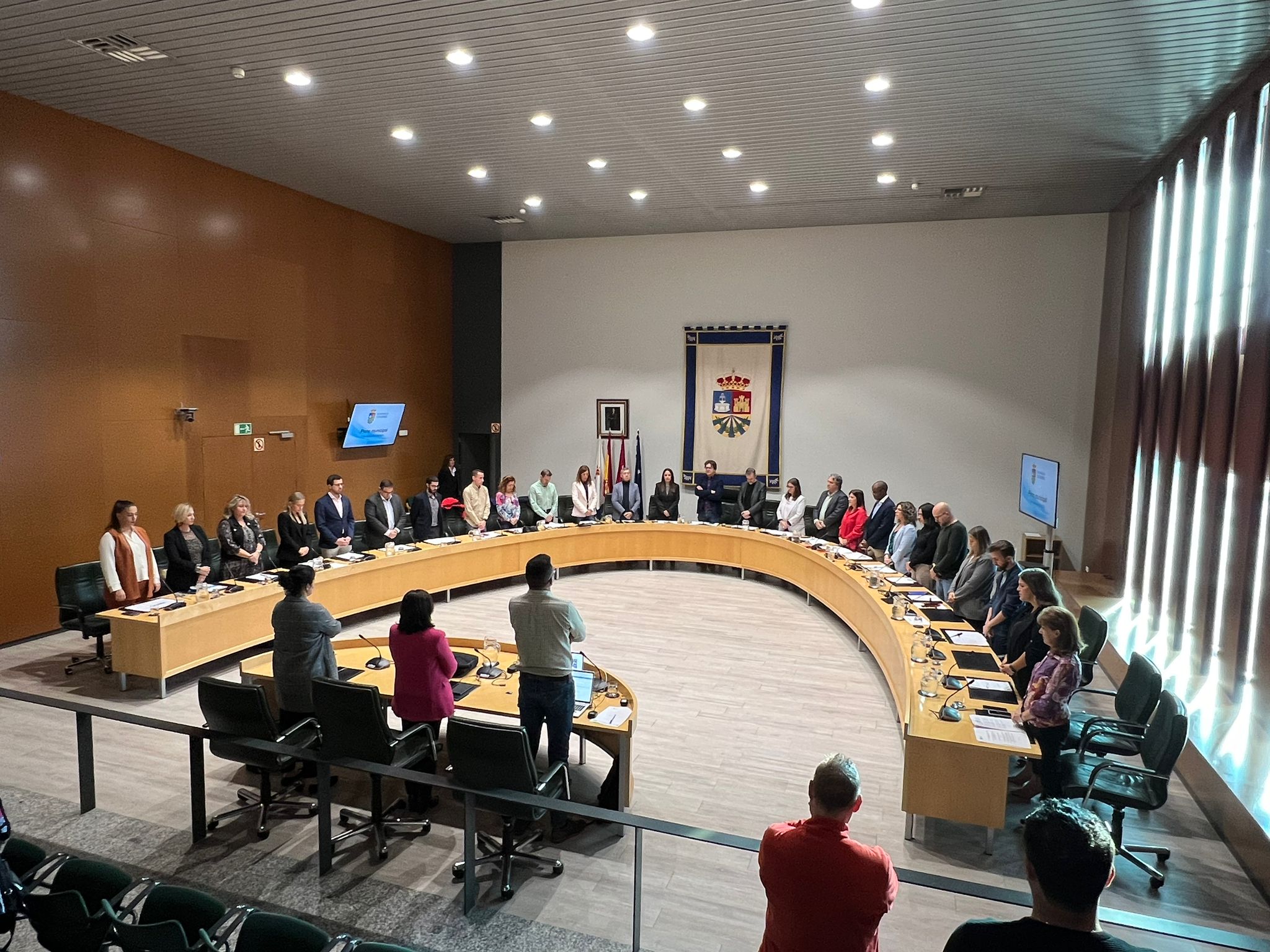 Concejales y público en la sesión plenaria en pie guardan minuto de silencio