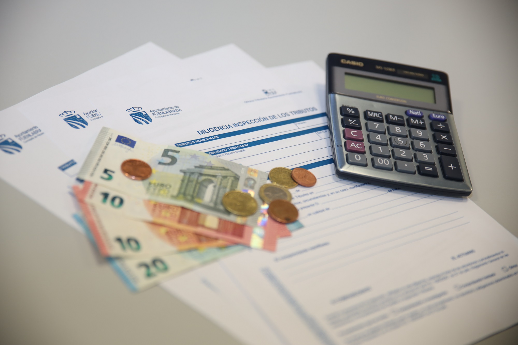 Calculadora y dinero sobre un formulario de tributos del ayuntamiento