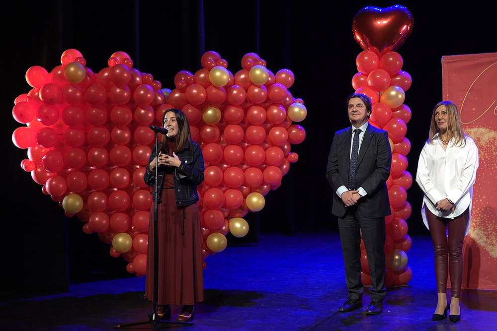 Dos mujeres y un hombre en un escenario con globos formando un corazón